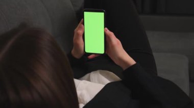 Green Mock-up Screen ile akıllı telefon kullanan bir kadının kanepeye uzanması. Cep Telefonu Chromakey kullanan kadın, İnternet Sosyal Ağ Tarayıcı, içeriği izleyen. 