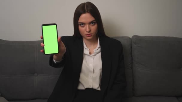 Wanita pengusaha Kaukasia cantik menunjukkan smartphone dengan kromakey layar hijau di sofa di rumah atau kantor. — Stok Video