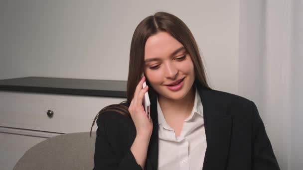 Улыбающаяся деловая женщина разговаривает по телефону в офисе. Портрет девушки разговаривающей по телефону на диване. Улыбающаяся женщина звонит в замедленной съемке. — стоковое видео