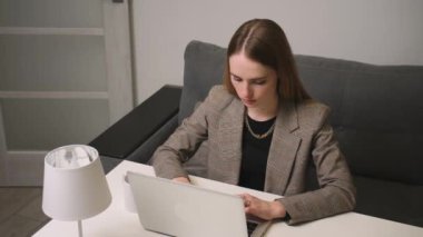 Dizüstü bilgisayar kullanan üzgün genç bir kadın sorun yüzünden kızgın, yazılım hatası yüzünden stresli, sosyal medyada kötü haber okumaktan endişeli evde kanepede oturuyor..