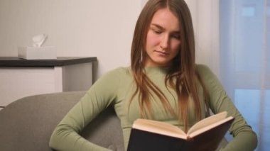  Oturma odasında kitap okuyan genç bir kadının portresi, öğrenme, öğrenme, eğitim, kitap okuma, evde kalma kavramı.