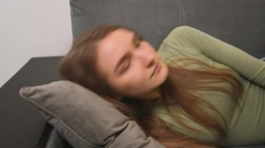 - Yakın çekim. Uykulu genç bir kadının portresi kanepeye düşüyor. Gülümseyen kadın evde tek başına uyuyor.. 