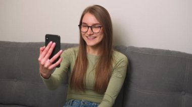 Akıllı telefondan video görüşmesi yapan gülümseyen kadın, kameraya el sallayan arkadaş canlısı kadın, evde telefonda görüntülü konuşma yapan güzel kadın..