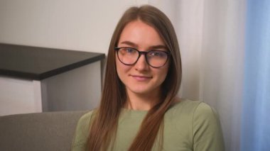Gözlüklü, güler yüzlü genç bir kadın ev ofisinde kameraya bakıyor. Mutlu güzel kadın yüzü kapalı alanda portre için poz veriyor..