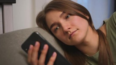 - Yakın çekim. Beyaz kadın portresi telefon kullanıyor, internette geziniyor, evdeki kanepede uzanmış içeriği izliyor..