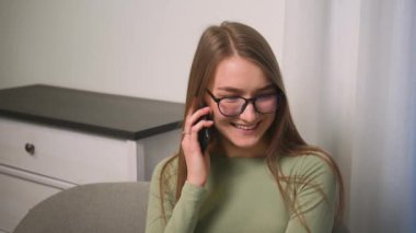 Gözlüklü gülümseyen kadının portresi evde akıllı telefonuyla konuşuyor arkadaşlarıyla iletişim kuruyor iyi haberler öğreniyor erkek arkadaşı ya da ailesiyle sohbet ediyor evdeki kanepede oturuyor..