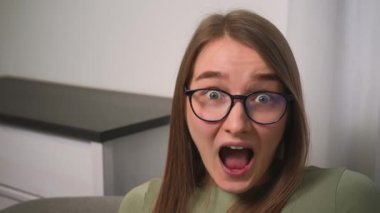 Gözlüklü, heyecanla gülümseyen genç bir kadının yakından portresi. Ağzını açarken hayretle 