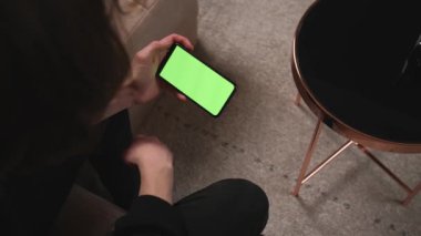 - Yakın çekim. Man at Home 'un Green Mock-up Screen ile Smartphone kullanarak bir koltukta oturması, Guy' ın Mobile Phone kromakey kullanarak içeriği izlemesi, İnternet Sosyal Ağ Taraması.