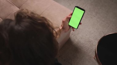 - Yakın çekim. Evdeki Adam 'ın Smartphone kullanarak bir koltukta oturduğu en üst görünümde Green Mock-up Screen, Guy' ın Cep Telefonu Chromakey kullanarak içeriği izlemesi, İnternet Sosyal Ağ Tarayışı var.