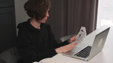 İnternetteki video konferansında konuşan adam ev ofisinde çalışıyor. Ev bilgisayarında görüntülü arama yapan yakışıklı bir işçi. Kağıtlarla çalışan adam.