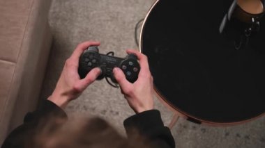Üst Manzara. Evdeki kanepede oturup video oyunları oynayan, elinde kumanda olan bir adamın yakın çekimi..