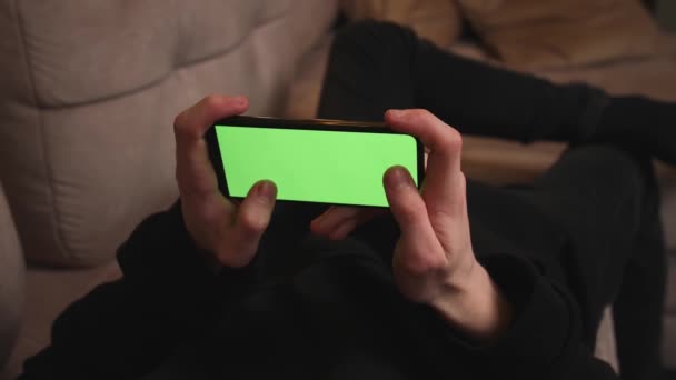 Fecha a porta. Homem em casa deitado em um sofá usando Smartphone com tela de Mock-up verde, Guy Usando jogos cromados de telefone móvel, Internet Social Networks Navegação. — Vídeo de Stock