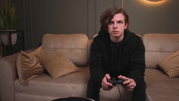 Enfocado joven caucásico hombre gamer holding joystick controlador jugando videojuegos sentado en sofá en casa. — Vídeos de Stock