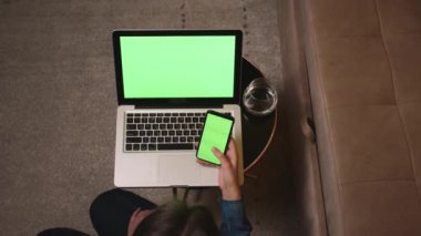 Üst Manzara. - Yakın çekim. Kadın evde dizüstü bilgisayar Chromakey kullanırken akıllı telefon yeşil ekranını tutuyor. Cep telefonu yeşil ekranı tutan kadınların yakın çekim görüntüleri.