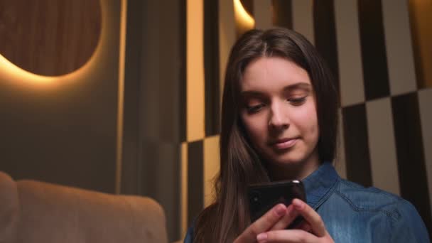 閉鎖だ。笑顔の若い女性の肖像は、自宅でソファの上に座ってソーシャルメディアでオンラインショッピングのための電話を使用して、技術のモバイルメッセージ通信遅い動き — ストック動画