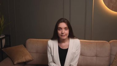 Agresif bir kadın kameraya bakarak konuşuyor. Ofisteki kanepede video konferansı yapıyor. Ev konseptinde görüntülü konuşma yapmak, web kamerası görüntüsü.