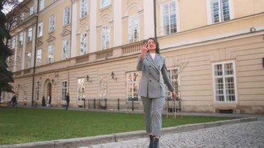 Güzel, gülümseyen bir kadın telefon görüşmesinde konuşurken sokakta yürüyor..