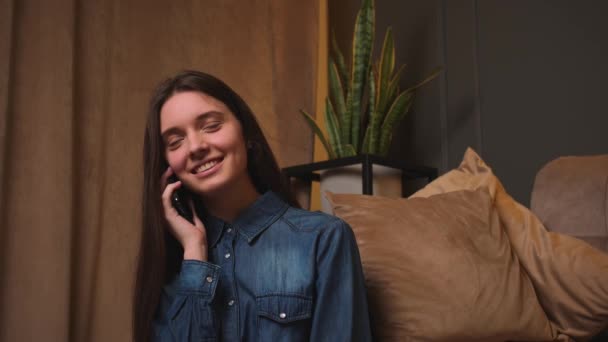 Smiling Woman talking on smartphone at home resting communicating with friends learns good news answers call chatting with boyfriend or family sitting on couch at home. — Stock Video