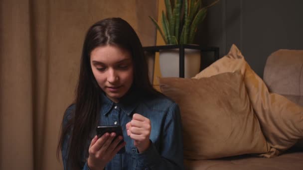 Mujer frustrada leyendo el mensaje en un teléfono inteligente. Chica molesta sentada en la sala de estar sosteniendo el teléfono móvil. Malas noticias, emociones, sentimientos, concepto de conversación — Vídeos de Stock