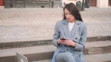 Sokakta telefon kullanırken merdivenlerde oturan genç kadın..