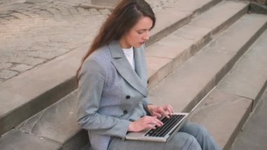Sokakta dizüstü bilgisayar kullanırken merdivenlerde oturan genç kadın..
