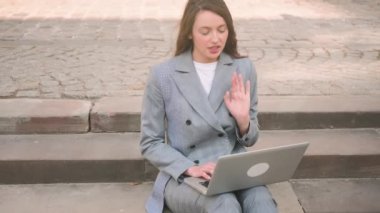 Genç kadın merdivenlerde oturmuş dizüstü bilgisayarla sokakta sohbet ediyor..