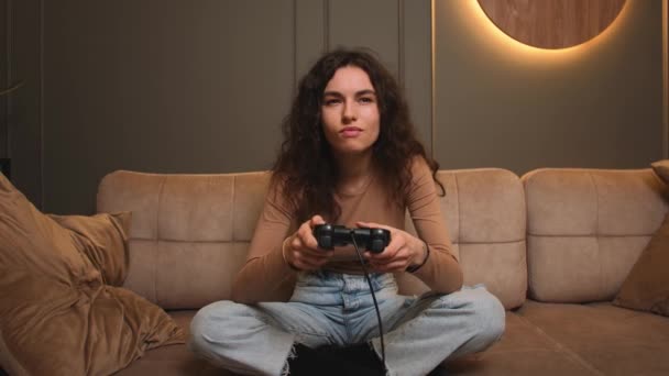 Mujer sonriente jugando un videojuego en casa. Emocionada mujer gamer sentada en un sofá, jugando videojuegos. Mujer celebra la victoria en el juego — Vídeos de Stock