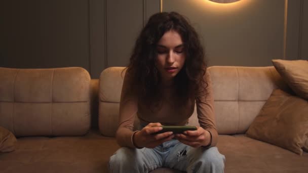 Telefonla cep telefonu oyunu oynayan bir kadın evdeki koltukta oturuyor. El, akıllı telefondaki oyun için dokunmatik ekrandır.. — Stok video
