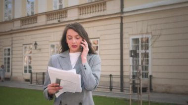 Sokakta kağıda bakarken telefonla konuşan bir kadın.
