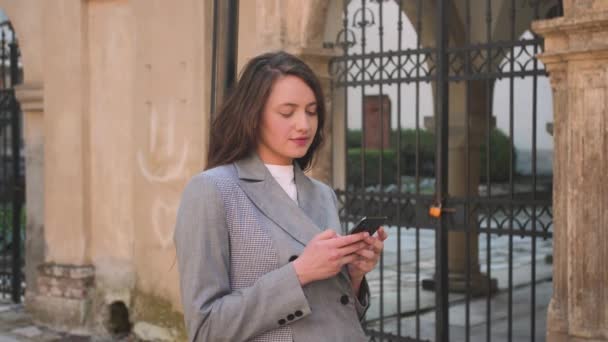 Mujer bastante sonriente escribiendo en el teléfono en la calle. — Vídeos de Stock