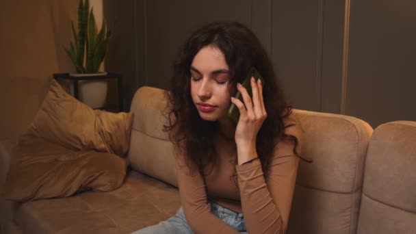 Stressed young woman talking mobile phone sitting on couch at home. — Stock Video