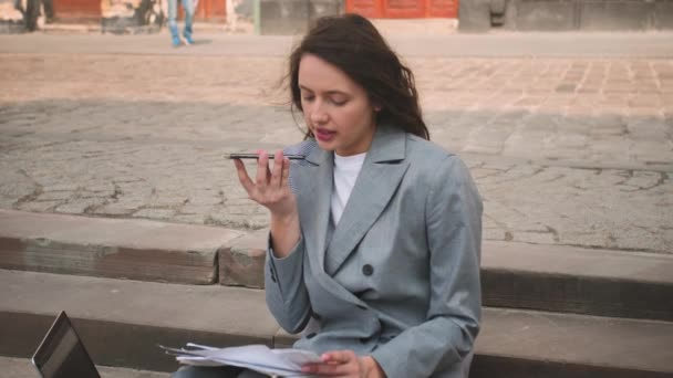 Jovem mulher sentada nas escadas enquanto falava ao telefone, trabalhando com documentos em laptop na rua. — Vídeo de Stock