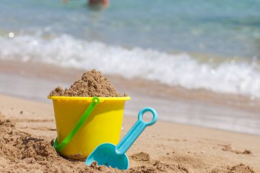 Çocuk kovası, kürek ve tropik sahildeki diğer oyuncaklar mavi gökyüzüne karşı