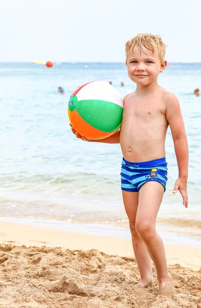 Menino segurando bola de praia colorida na praia desfrutando de férias de verão — Fotografia de Stock