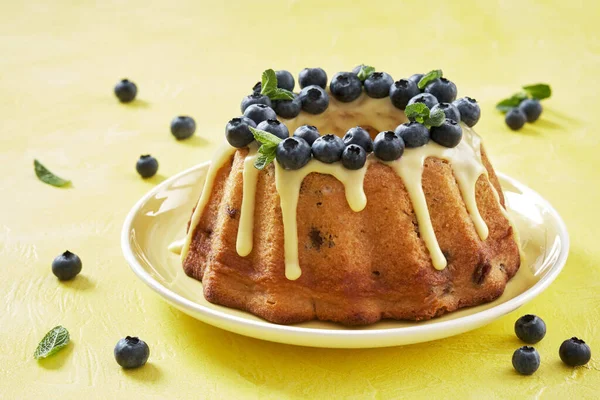 Blueberry bundt cake with icing on a yellow background — Stock Photo, Image