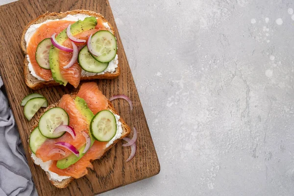Zdrowe tosty z chlebem żytnim z serem śmietankowym, łososiem, świeżym ogórkiem i czerwoną cebulą — Zdjęcie stockowe