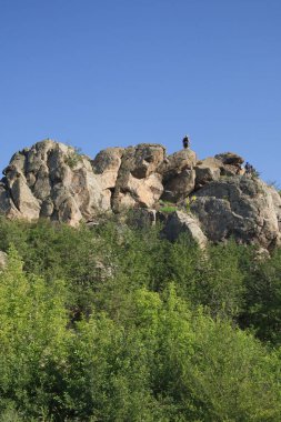 Sıcak bir yaz gününde kayalık bir tepenin tepesine tırmanmak. Bulutsuz mavi gökyüzü bir kayanın tepesinde.