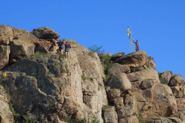 Migia, Ukrayna, 28 Haziran 2020. Güneşli bir günde dağın tepesinde bir grup dağcı. Tepenin tepesinde bayraklar. Dağların tepesinde bulutsuz mavi gökyüzü.