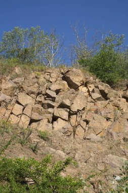 Sıcak bir yaz gününde Ukrayna 'nın Nikolaev bölgesinde terk edilmiş bir granit ocağının kayalık yamacı. Keskin taşlar seyrek bitkilerle kaplanmış. Uçurumların üzerinde bulutsuz mavi gökyüzü.