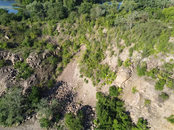 The rocky slopes of the hill are overgrown with bushes and small trees. Rocky terrain, aerial view.