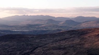 İrlanda kırsalının dramatik hava görüntüsü. Yuvarlanan tepeler ve uzak dağlar resim gibi bir manzara yaratıyor. Bunu bir sonraki seyahat tanıtımında kullan..
