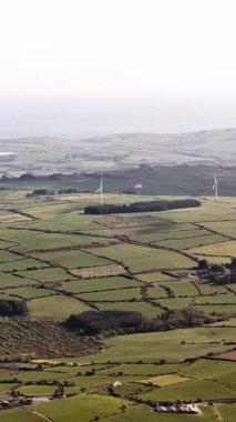 Güneşli bir günde tarlaları, rüzgar türbinleri ve kıyı şeridi olan İrlanda kırsal manzarası.