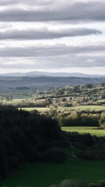 Bulutlu bir gökyüzünün altında yuvarlanan tepeler. yemyeşil alanlar ufka kadar uzanıyor.