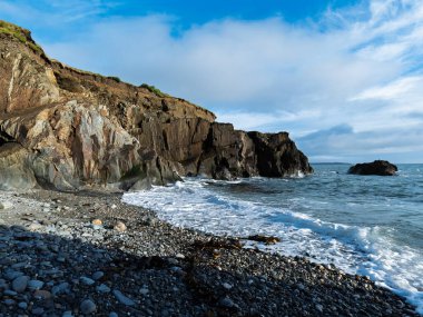 Huzurlu okyanus manzarası. Çakıl taşı plajı bulutlu bir gökyüzünün altında dalgaların dokunduğu yer..
