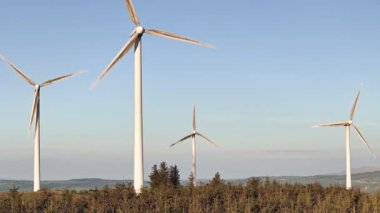 West Cork, Ireland, May 5, 2025. Multiple wind turbines on a hilltop covered with trees, spinning in the breeze. A powerful visual for sustainability themes.