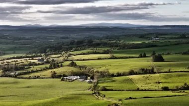 Batı Cork, İrlanda 'da yemyeşil çayırlara ve yuvarlanan tepelere tepeden bakan. Evler manzarayı çarpıcı bir gökyüzünün altında dağınık bulutlarla dolduruyor..