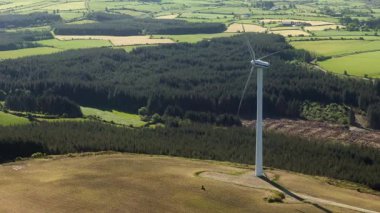West Cork, İrlanda, 5 Mayıs 2025. Bir rüzgar türbini elektrik üretiyor. Gündüz boyunca İrlanda kırsalında bir orman ve tarım arazisi yakınında yer alır. Temiz, yenilenebilir enerji burada üretilir..