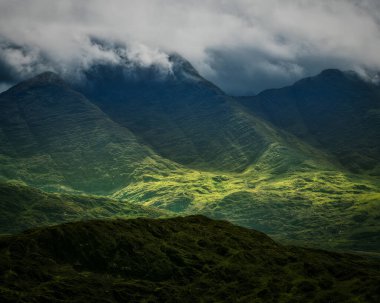 Coomloughra at nalı patikası boyunca yapılan yürüyüş sırasında bulutlarla kaplanmış yeşil dağların güzel bir manzarası. Alt vadilerde ışık parlıyor ve çarpıcı bir kontrast oluşturuyor..