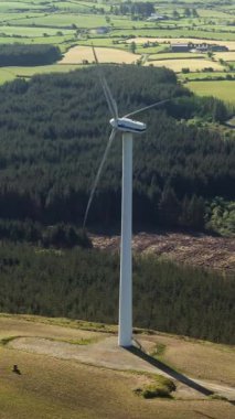 West Cork, İrlanda, 5 Mayıs 2025. Rüzgar türbini, gün boyunca İrlanda 'nın yeşil kırsalında, ormanın yanında duruyor ve sürdürülebilir yenilenebilir enerji yaratıyor..