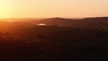 Gün batımında resimli bir manzara izleyin. Tepeler, küçük bir göl ve rüzgar türbinleri altın saat boyunca görülebilir..